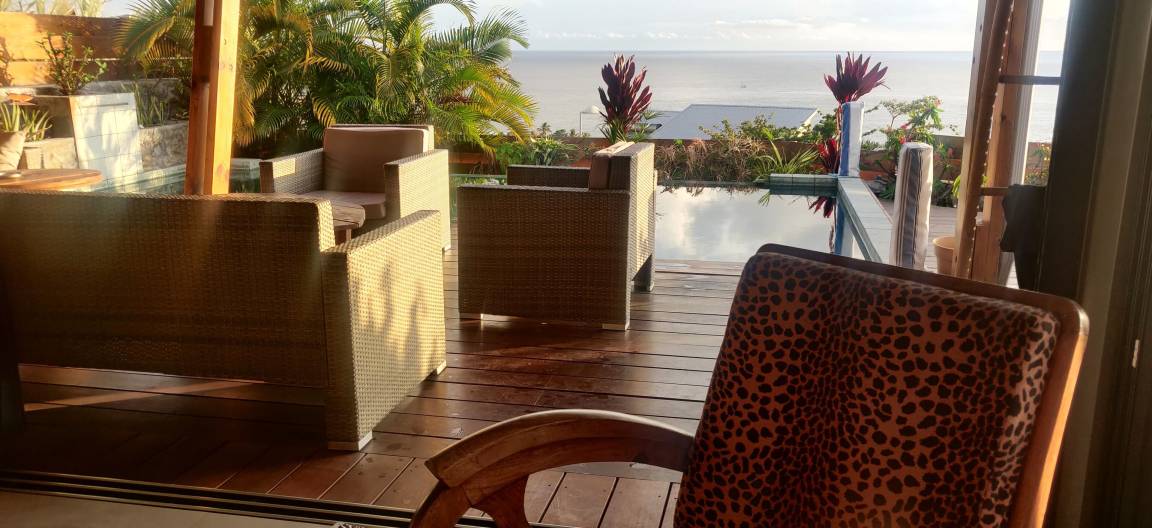 Fauteuils en rotin sur la terrasse en bois face à la piscine et à l'océan