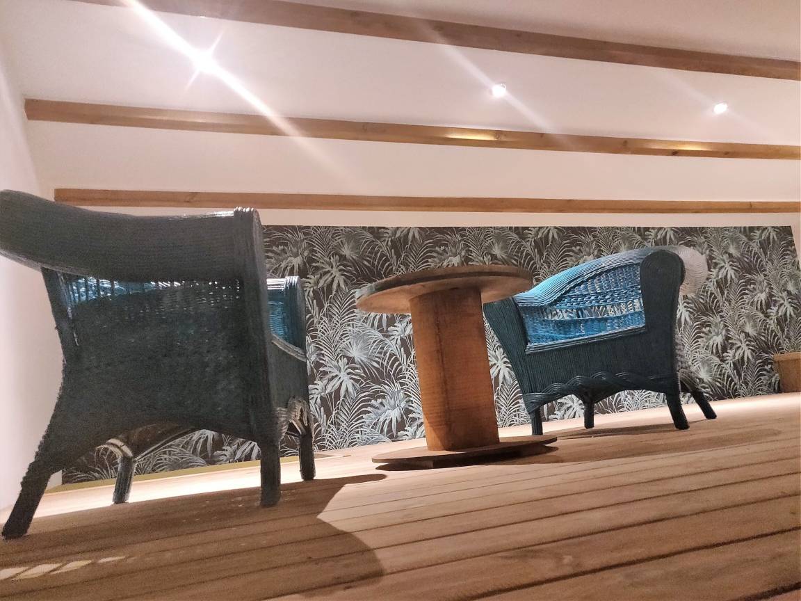 Espace détente en mezzanine avec fauteuils en rotin bleu et papier peint tropical